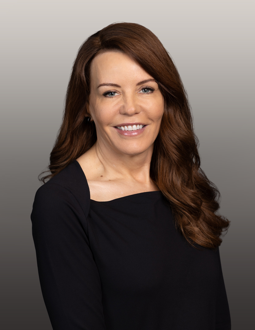 Professional headshot of a woman in a dark dress smiling in front of a neutral background.